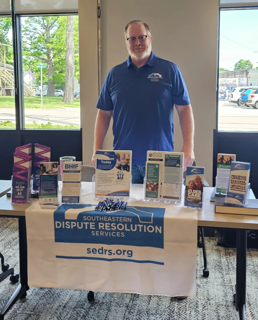 Executive Director Marc Stanley stands behind a table with displays of brochures.